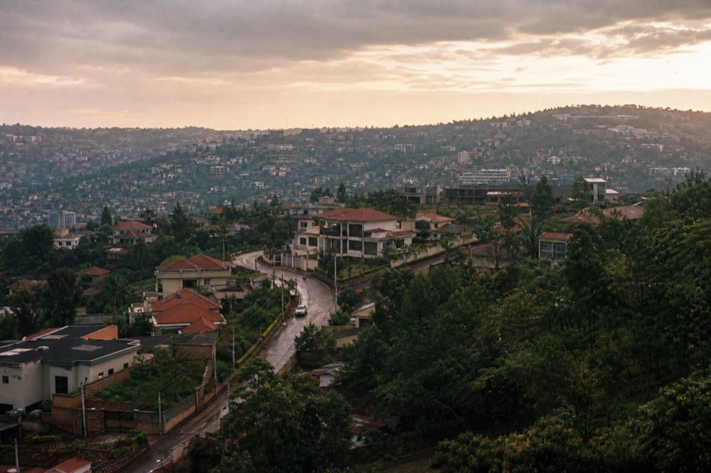 Aerial view of Kigali at golden hour, low modern buildings spread across green ridgelines with red-tiled roofs and winding tarmac roads between them