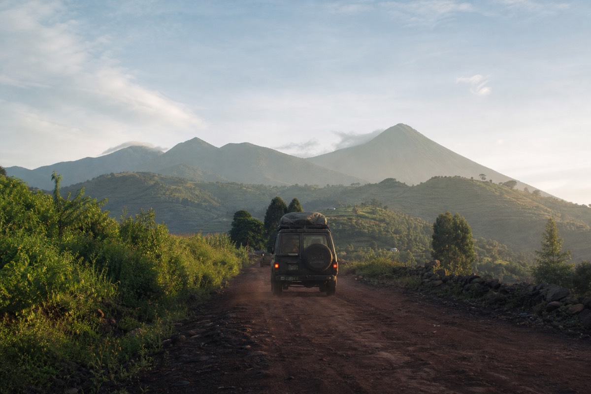 A 4x4 on a red-dirt road heading toward the Virunga volcanoes at dawn